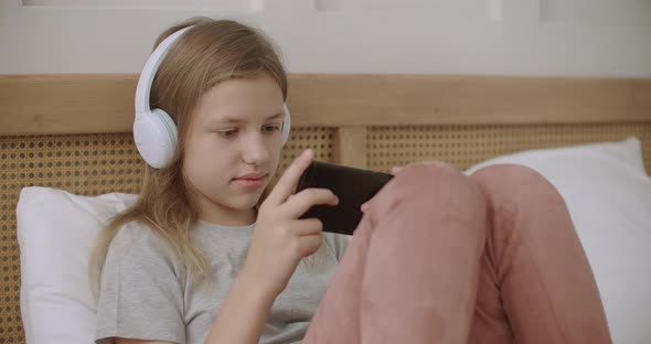 School Girl Is Viewing Funny Video on Display of Smartphone and Listening By Headphones in Her