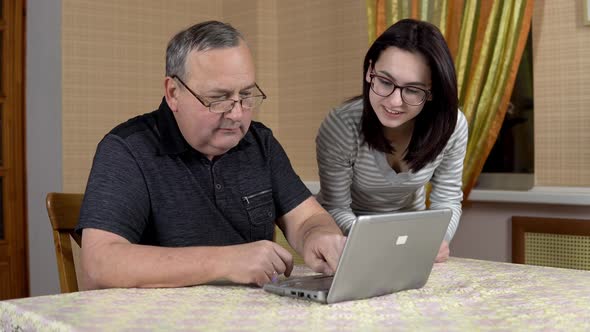 Daughter Teaches Father How To Use a Laptop. A Young Woman Shows Her Old Father Where To Click