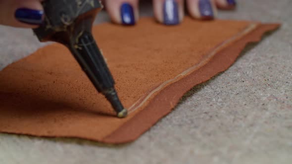 Closeup of Worker Hands Applying Glue on Edge of Leather Piece Indoors