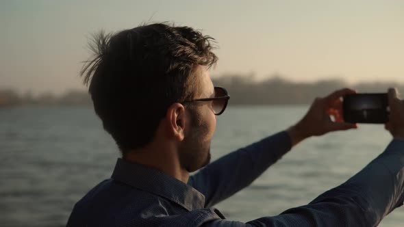 Man Hands Holding Mobile Phone And Taking Picture At Sunset. Guy Taking Photo of Sunset With Mobile.