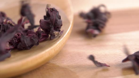 Falling dry hibiscus flowers into a rustic wooden spoon in slow motion