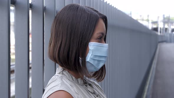 Young elegant woman leaning against a metal grille with a hygienic respirator mask over her nose and