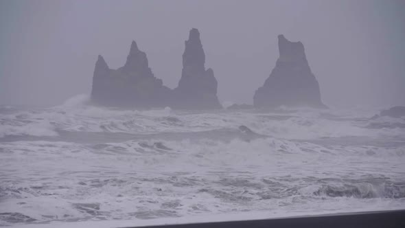 Static, Slow motion shot, of waves hitting a black sand beach and cliff, on the arctic sea, on a clo