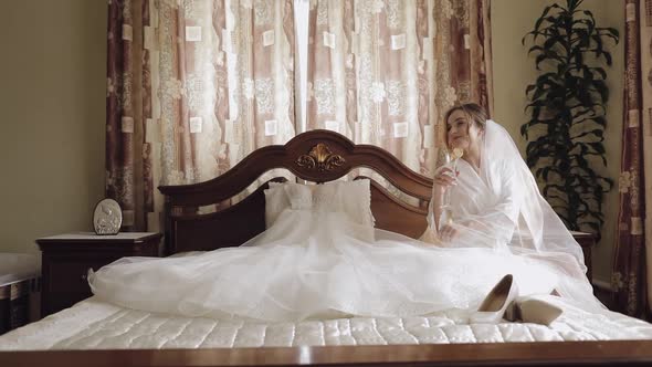 Beautiful and Lovely Bride in Night Gown and Veil Sitting and Drinking Champagne