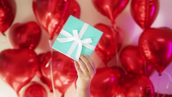 Love Concept Female Hand with Blue Box White Ribbon at Red Balloons Background