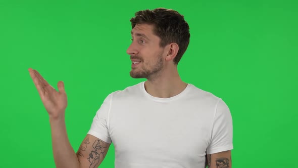 Portrait of Confident Guy Is Talking and Pointing Side Hand for Something, Copy Space.. Green Screen