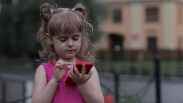 Child Girl Talking By Smartphone Outdoors. Kid in Pink Dress Talking By Mobile Phone on City Street