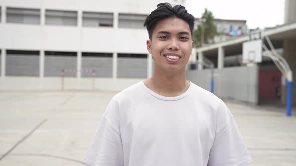 Portrait of Young Smiling Asian Male College Student with White Tshirt in the Basketball Yard of