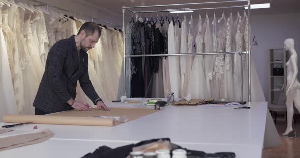 The Tailor Drawing a Curve on Fabric on a Desktop in Dress Atelier