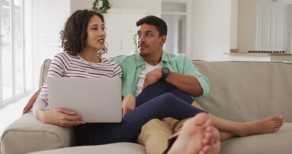 Hispanic couple sitting on sofa looking at laptop discussing
