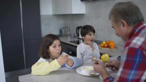 Two Small Children are Eating Sandwiches Made By Grandfather