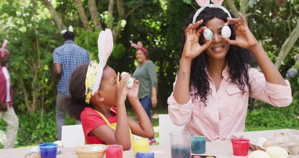 Animation of happy african american mother and daughter painting easter eggs outdoors, having fun