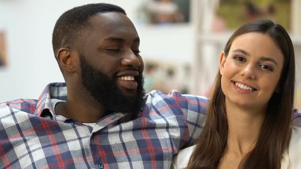 Black Man Looking at His Pretty Girlfriend, Couple Sitting on Sofa and Hugging