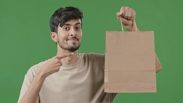 Portrait Young Smiling Guy Holding Paper Package Pointing Finger to Shopping Bag Hispanic Male Buyer