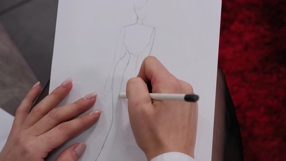 Closeup of a Fashion Designer Girl Drawing a Sketch of a Dress with a Pencil