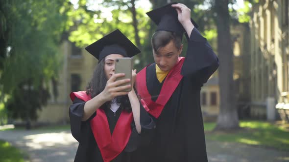 Satisfied Couple of Graduate Students Taking Selfie on Smartphone Standing at University Campus