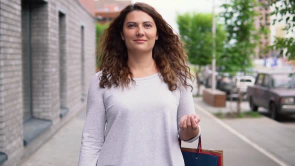 A Girl in a Light Dress with Long Hair Goes Down the Street After Shopping Having a Good Mood and