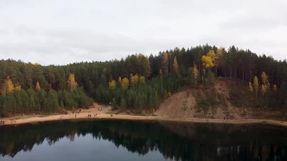 Aerial drone view of a colourful autumn forest next to a lake with sandy banks. Recorded in Ogres Zi