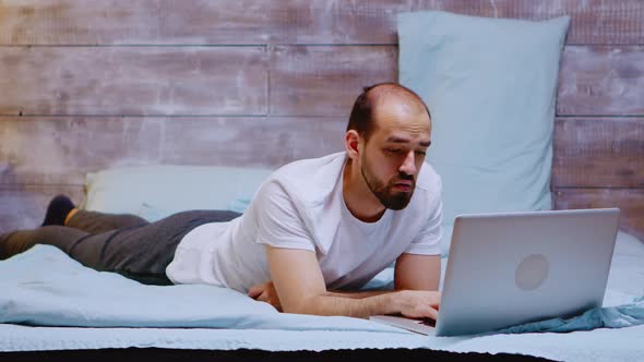 Young Adult Lying in His Bed Working on Laptop Late at Night