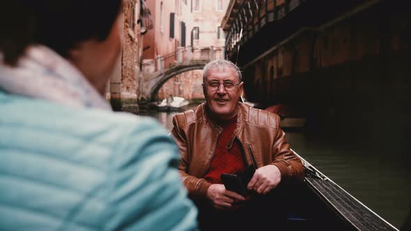 Happy Smiling Senior European Male Tourist Listening To Older Woman in Gondola During Venice Canal