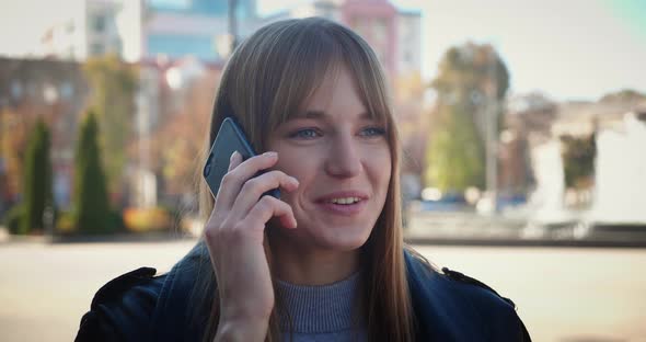 A Young Blonde with Blond Hair Speaks on the Phone While Standing on the Street