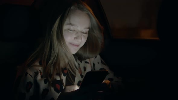Young Smiling Woman in the Backseat of a Car and Texting Somebody