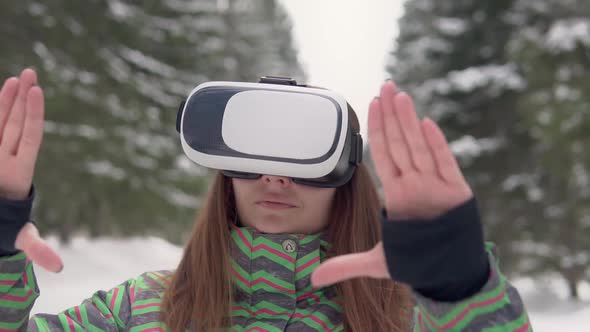 A Young Woman Uses Electronic Virtual Reality Glasses on the Street in a Snowy Forest. Slow Motion