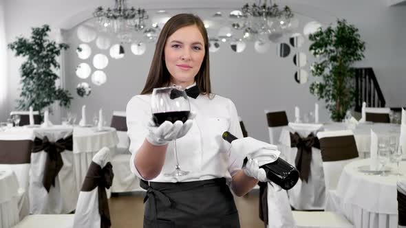 Female Waiter in White Gloves Holds a Glass and a Bottle of Red Wine