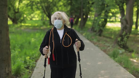 Active Senior Old Woman in Mask Training Nordic Walking in Park at Quarantine