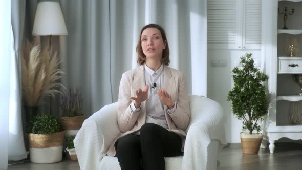 Smiling young woman, blogger, vlogger, influencer, sitting at home, talking, looking at the camera