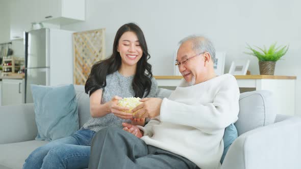 Asian senior father and daughter watch funny movie together at home.