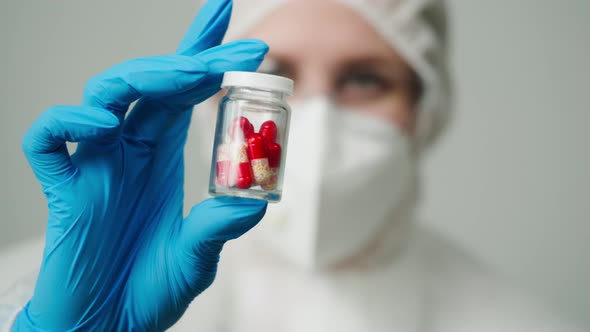 Closeup of Doctor in Protective Medical Uniform Nurse Wearing Mask Glasses and Gloves Holding Bottle