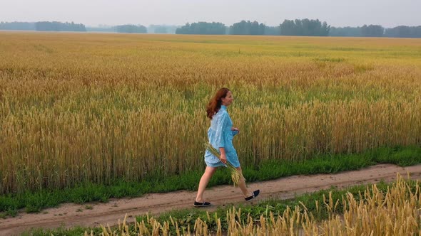 A Young Girl in a Dress Walks Along a Wheat Field