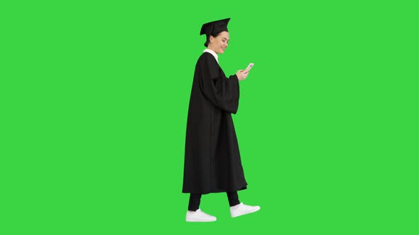 Smiling Female Graduate in Mortarboard Texting on Her Phone While Walking on a Green Screen, Chroma