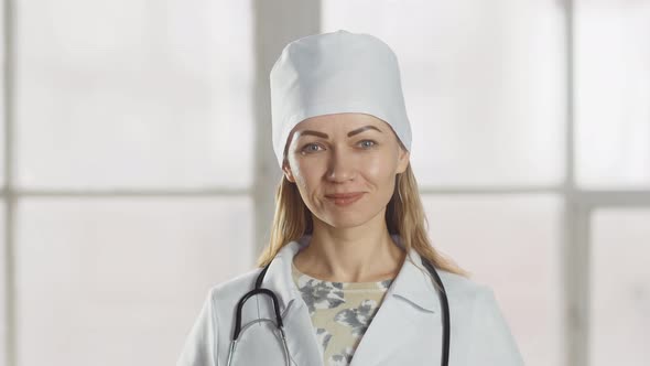 A female doctor smiles and nods her head approvingly at the camera. Professional female doctor in un