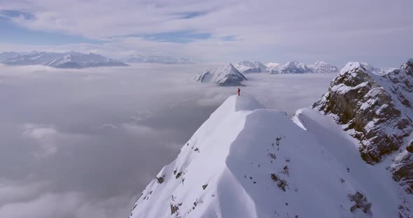 Aerial drone view of a mountain climber skier on the peak summit top of a snow covered mountain.