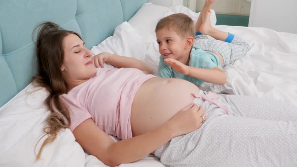 Happy Smiling Pregnant Woman with Little Boy in Pajamas Lyin in Bed and Talking