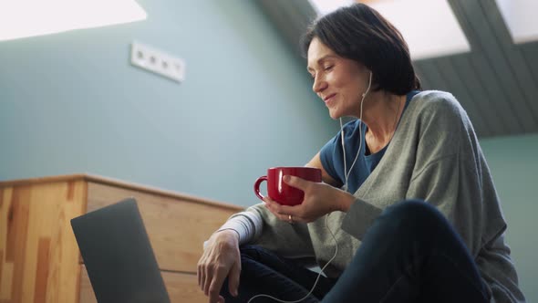 Happy mature woman looking at laptop and drinking tea