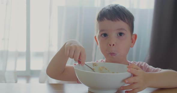 Cute Baby Boy Eat His Own Oatmeal Sitting on the Couch at Home