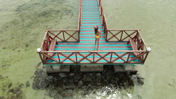 Sexy Brunette Woman in Yellow Bikini Walking on Wooden Bridge