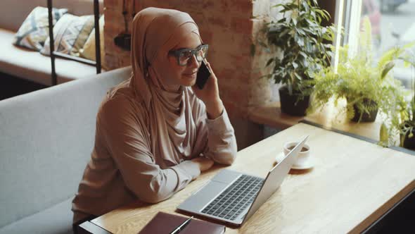 Muslim Businesswoman in Hijab Talking on Mobile Phone in Cafe