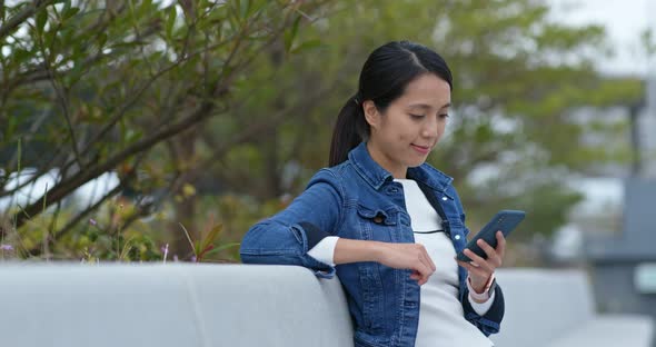 Woman Look at Mobile Phone and Sit on The Outdoor Bench