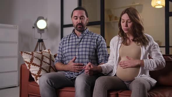 Pregnant Couple Doing Breathing Exercise on Sofa