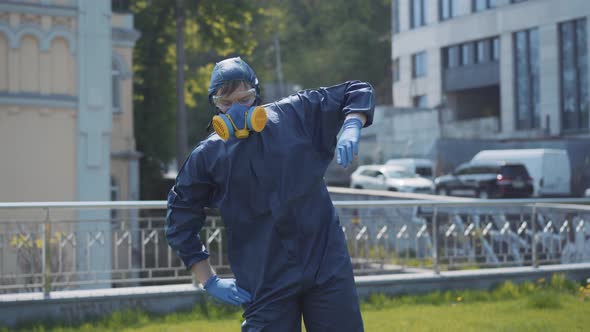 Funny Workout of Man in Respirator and Chemical Suit Outdoors. Portrait of Young Caucasian Sportsman