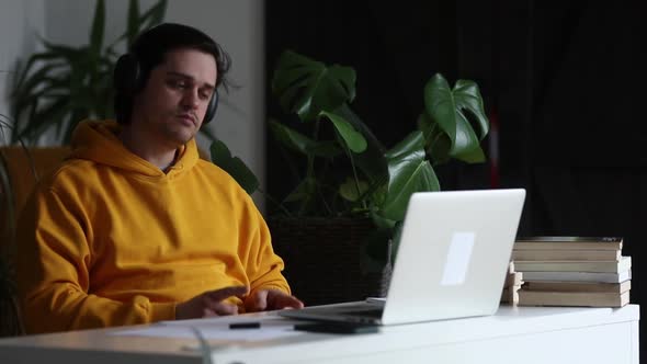 Man working at home office at laptop and listen a music in headphones