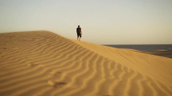 Man Walking Along Top Of Rippled Sand Dune