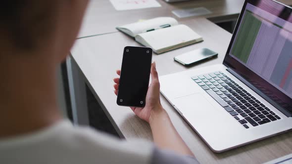 Mixed race businesswoman sitting at desk and using smartphone with copy space on screen in office