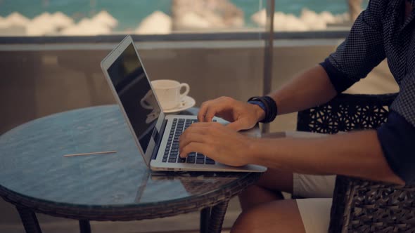 Man Working On Laptop In Vocation.Freelancer Works Outdoors On Computer.Drinking Coffee On Sea.