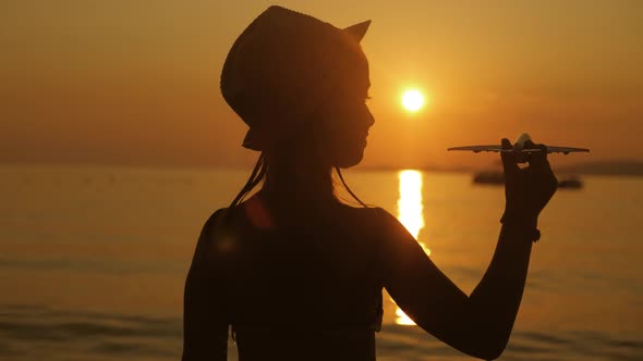 Silhouette Girl Plays with a Toy Airplane on Tropical Beach at Sunset. Hand with Small Plane Close