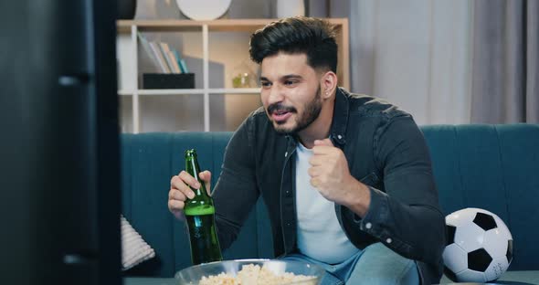 Man Sitting on the Couch at Home in front of TV Set and Watching Football match